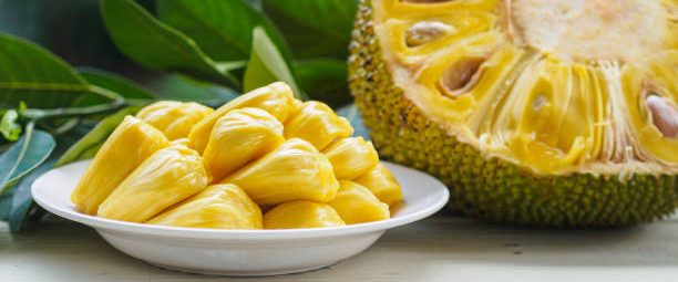 Fresh Jack fruit in white dish, half of jack fruit and jack fruit leaf on wooden table.